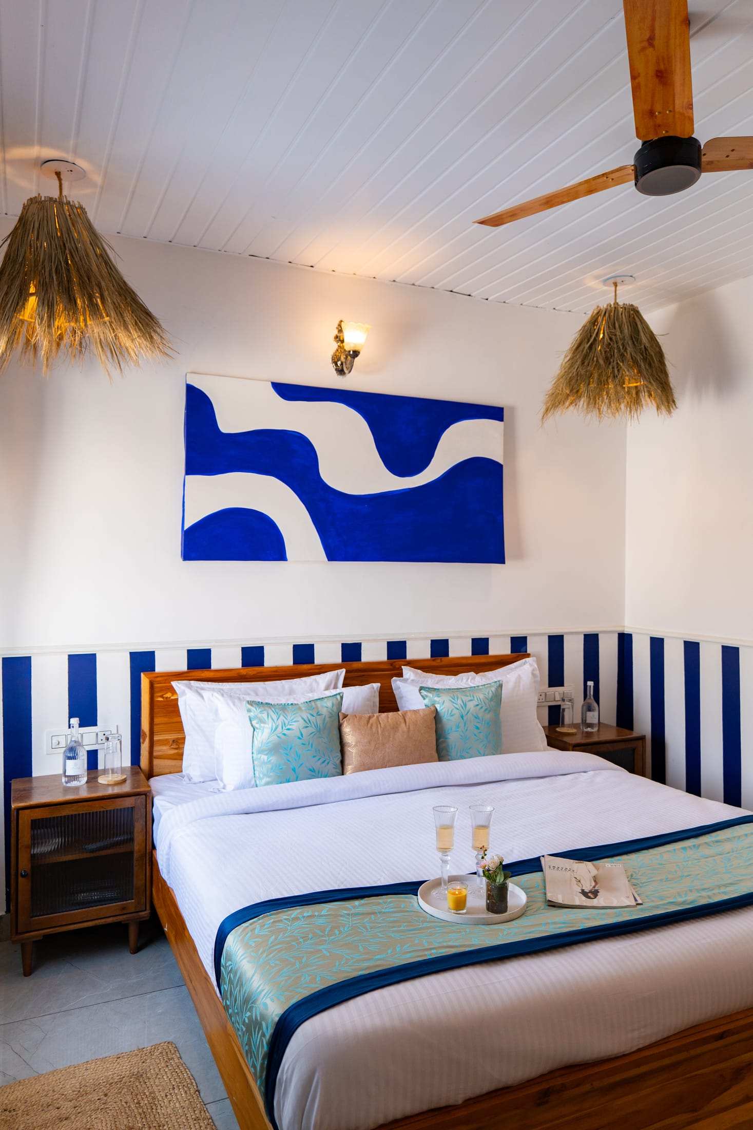 King bed dressed in teal and peach cushions beneath blue artwork