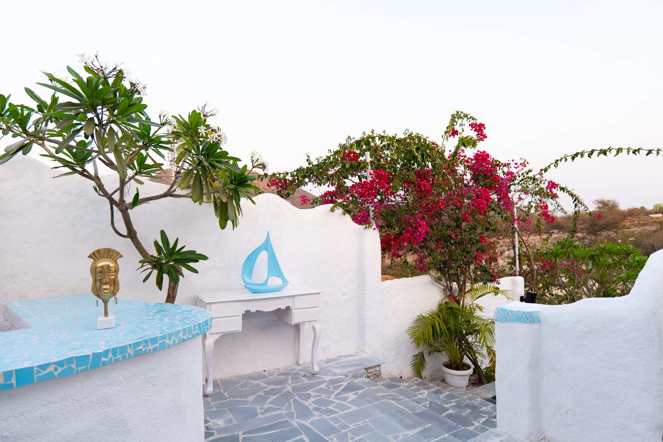 Terrace corner with a blue sailboat cut-out, white console and pink bougainvillea