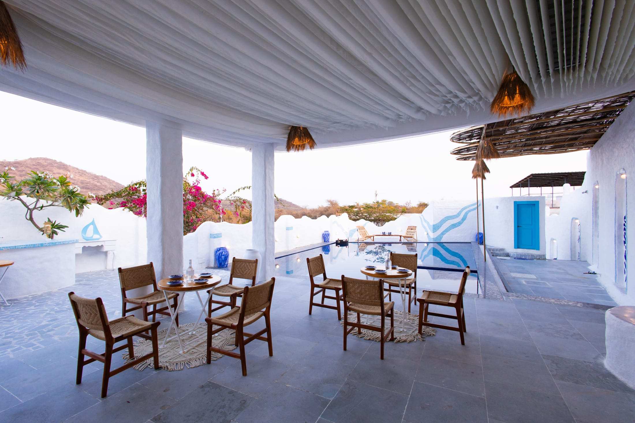 Dining sit-out with white pillars and draped fabric overlooking the pool
