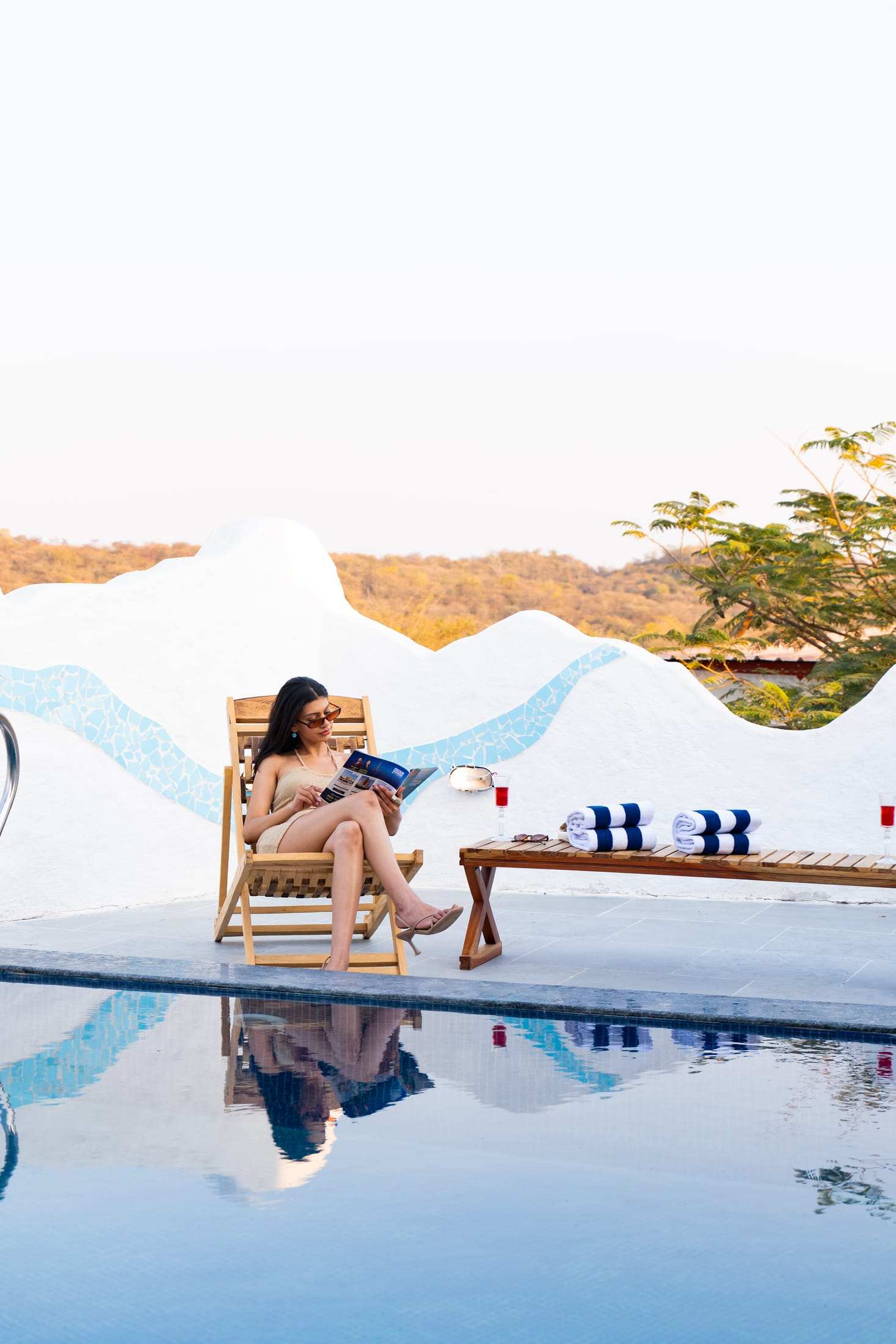 A guest reading on a wooden lounger beside the pool at sunset