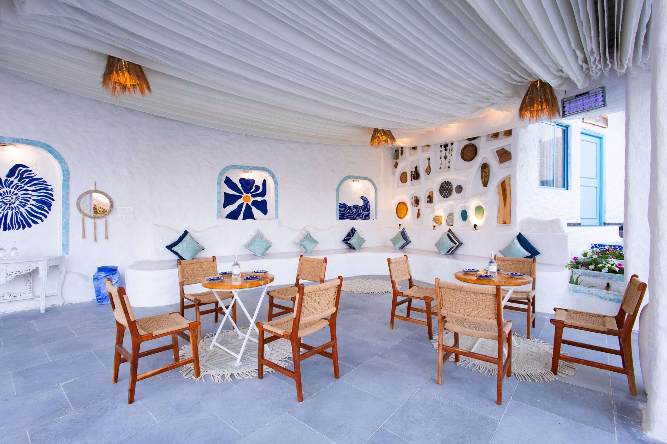 Open living and dining sit-out with cane chairs, blue and white decor and curved walls