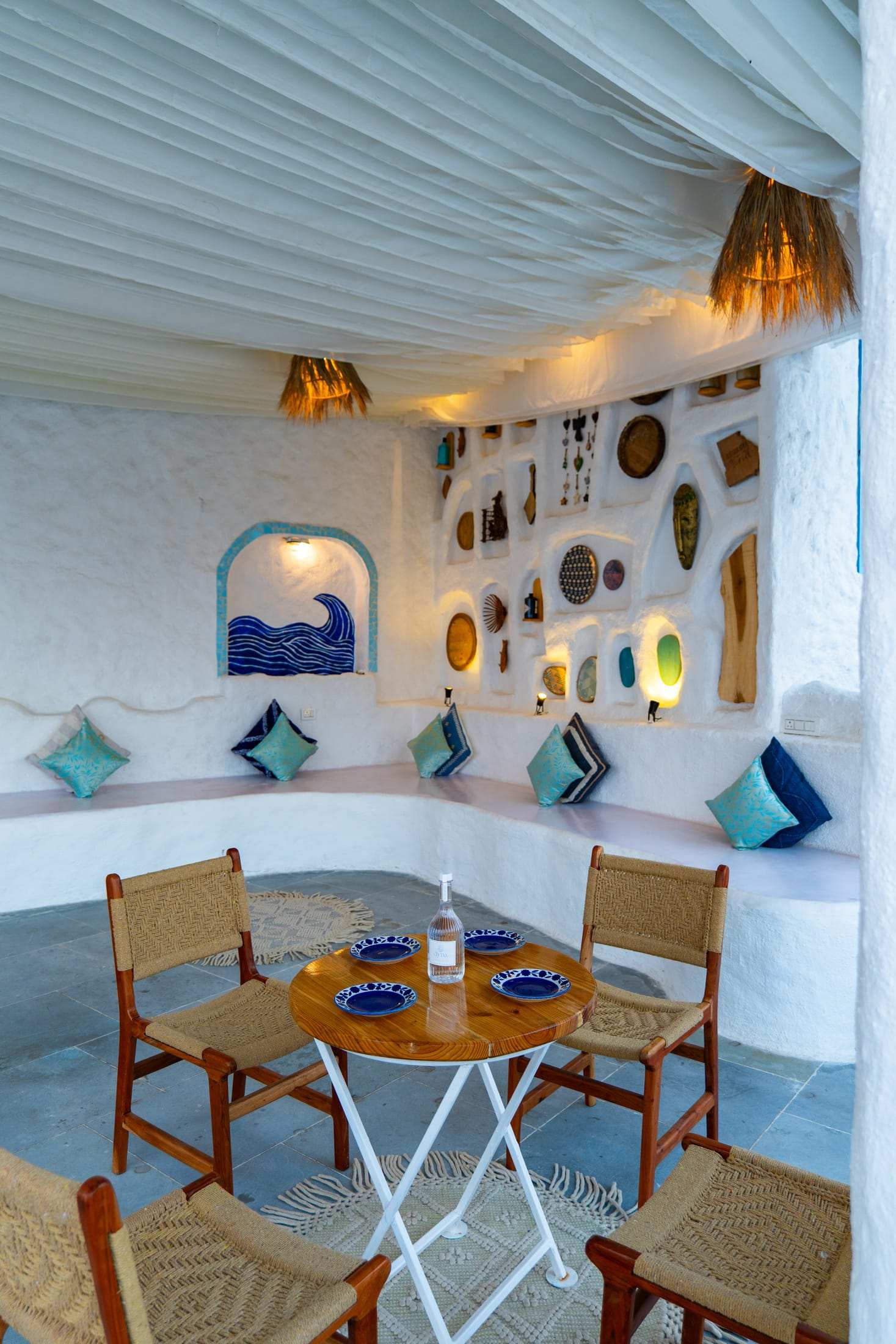 Built-in white seating with teal cushions under a wave mural niche and lit wall decor