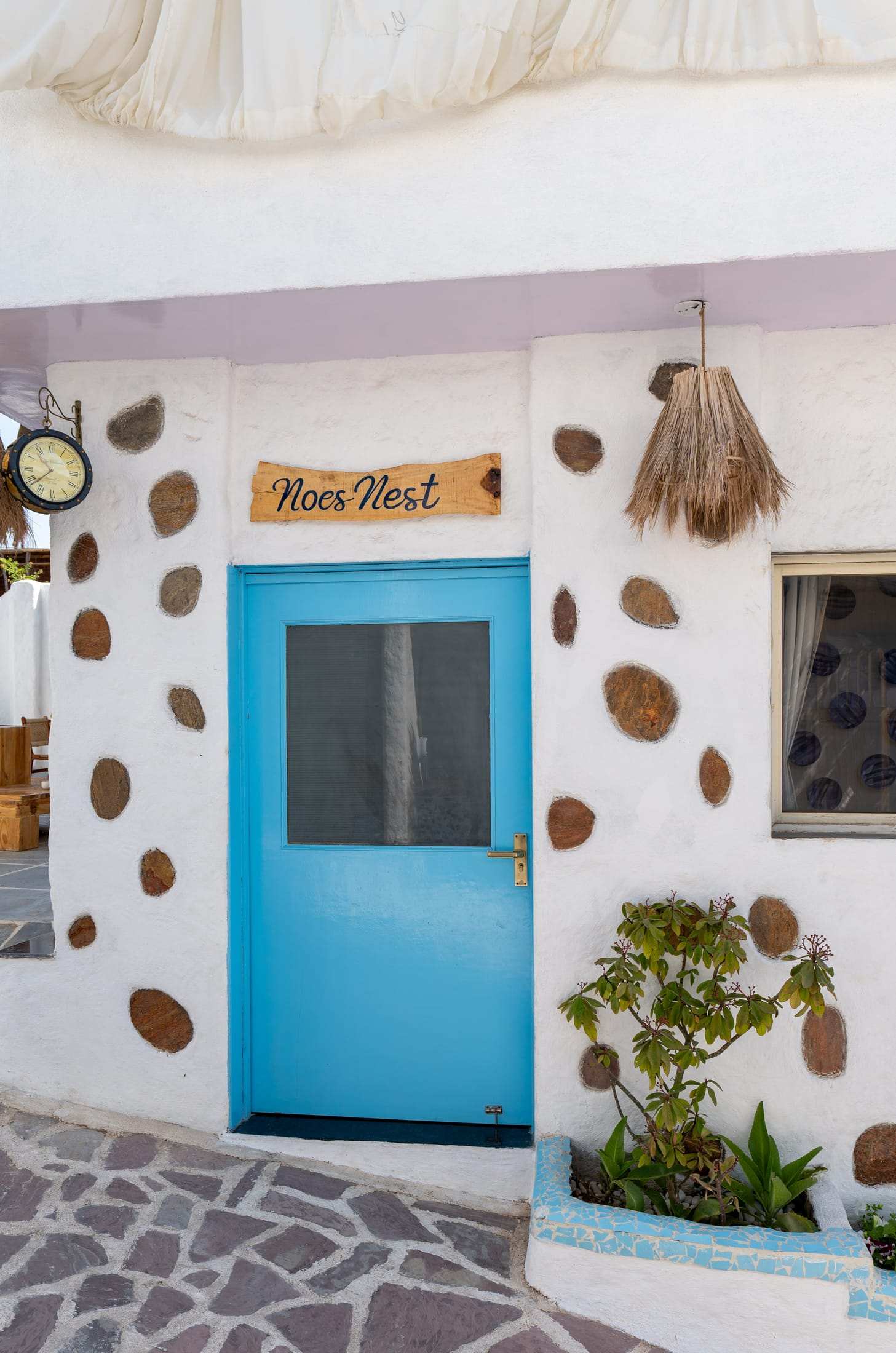 Entrance to Noe's Nest: a blue door set in a white wall studded with stone discs