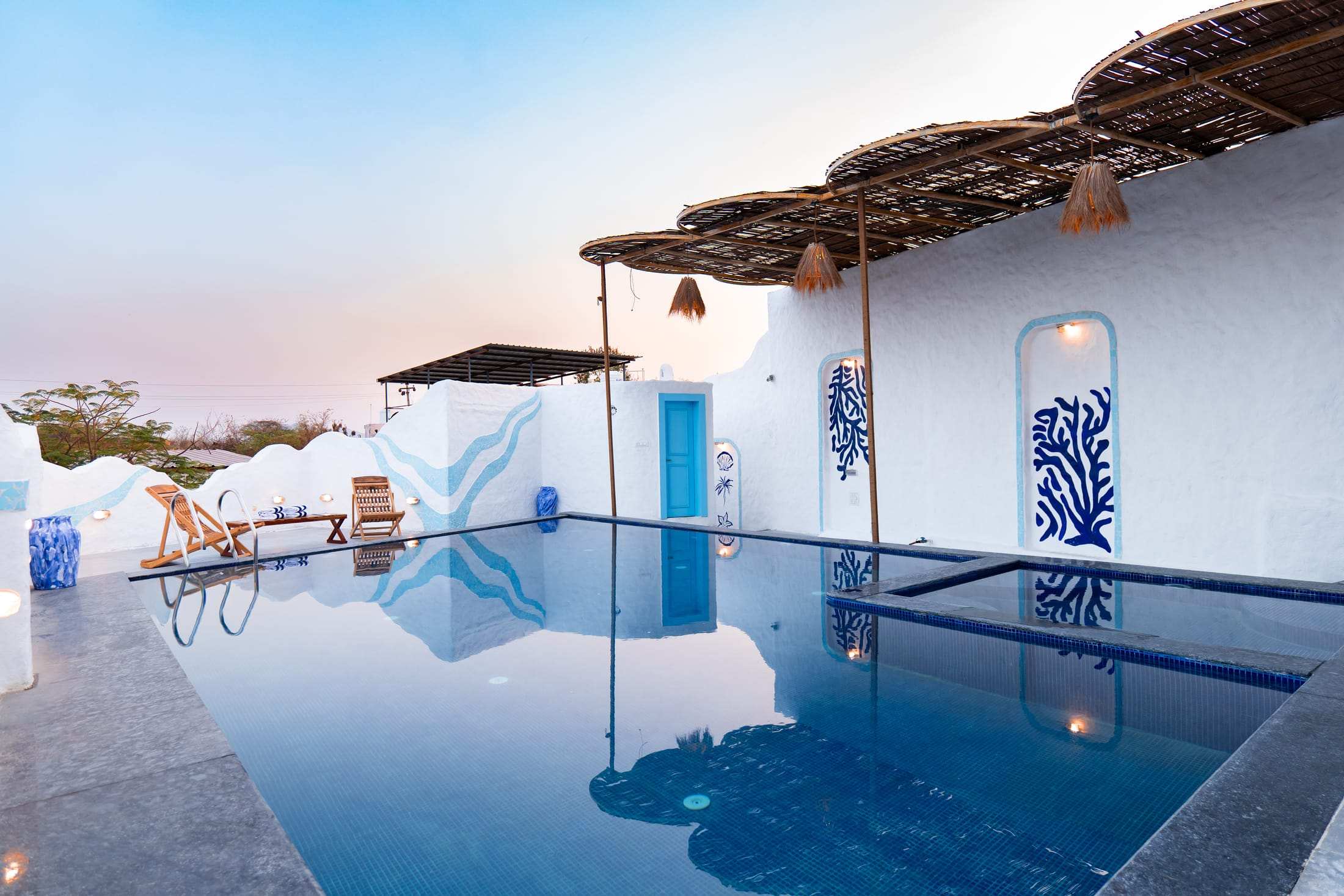 Pool at dusk with the thatched pavilion, blue door and coral mural