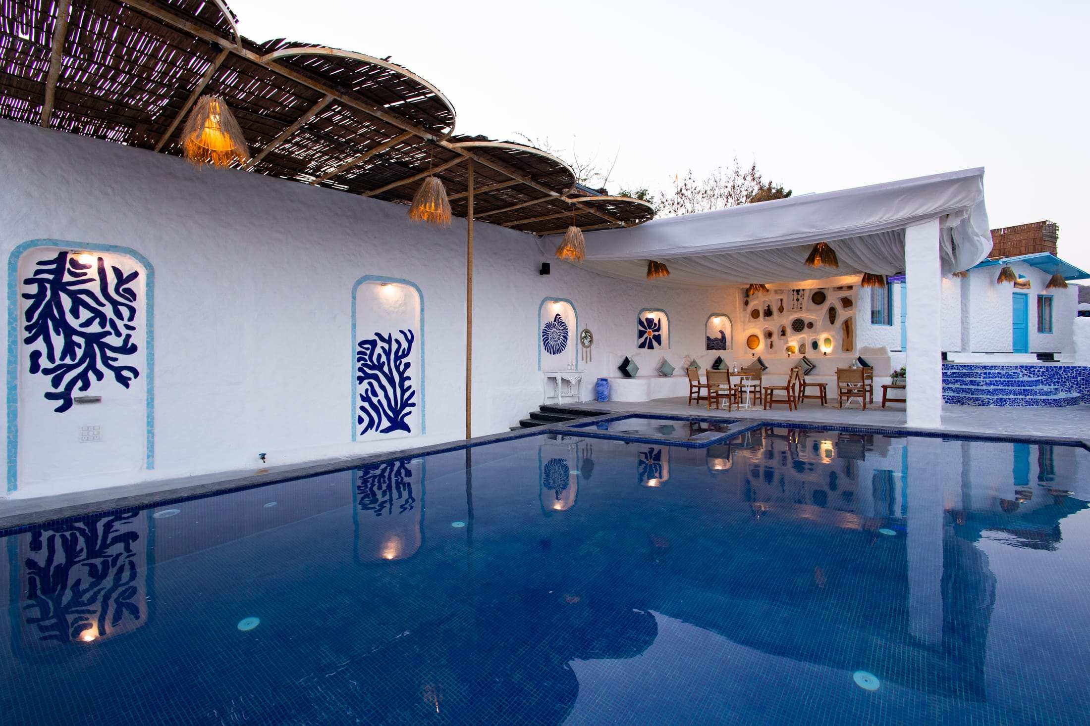 Pool at dusk reflecting the white pavilion, blue coral mural and warm lights