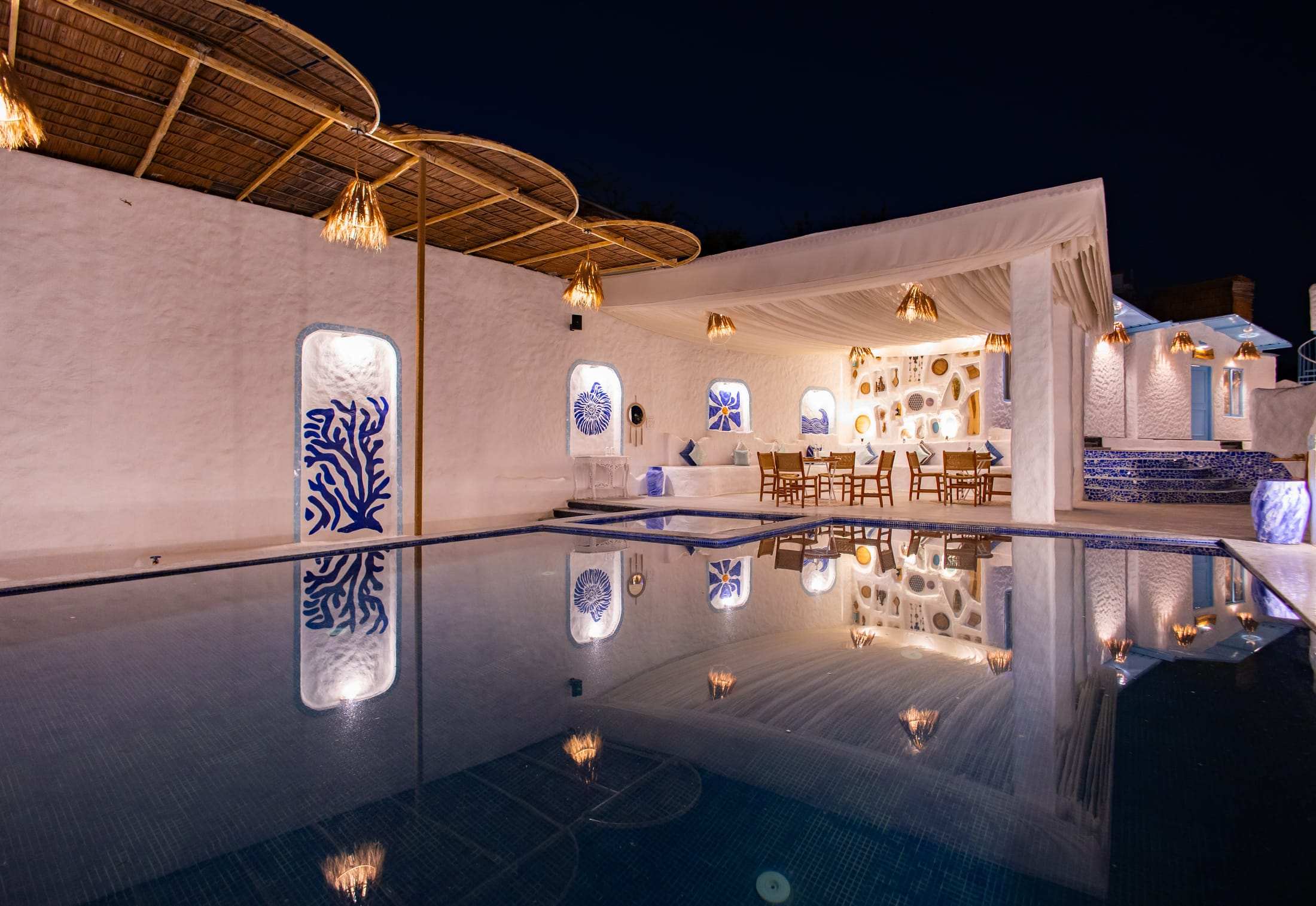 Pool at night with the lit pavilion and white walls reflected in the water