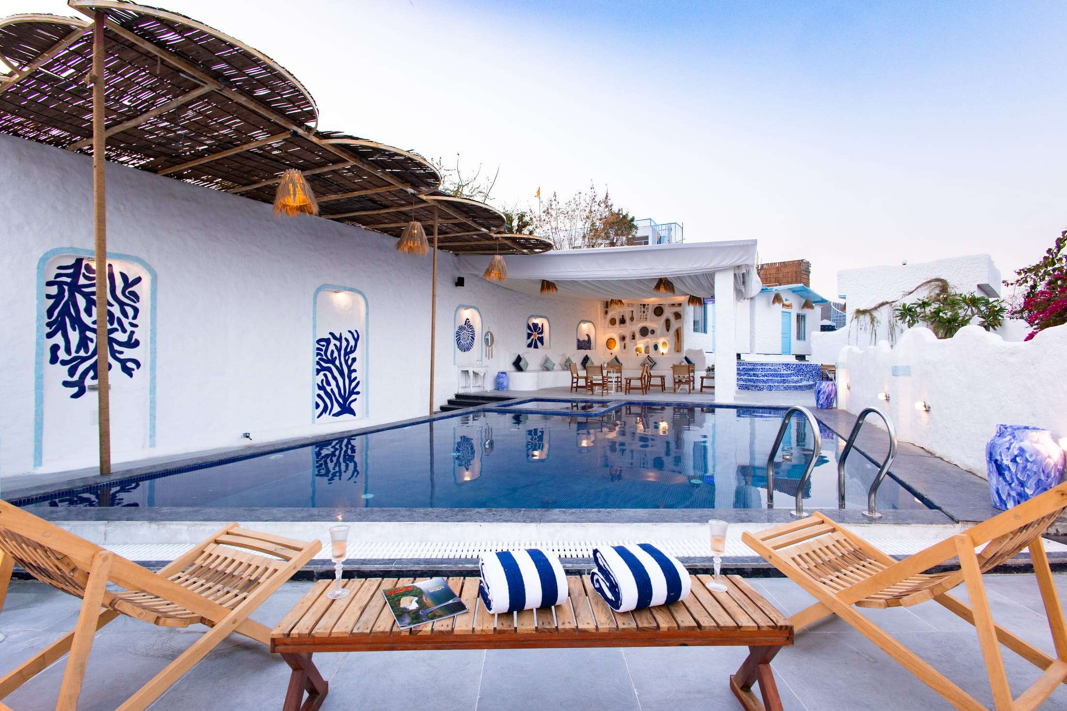 Wooden sun loungers and striped cushions beside the pool with the blue and white pavilion behind