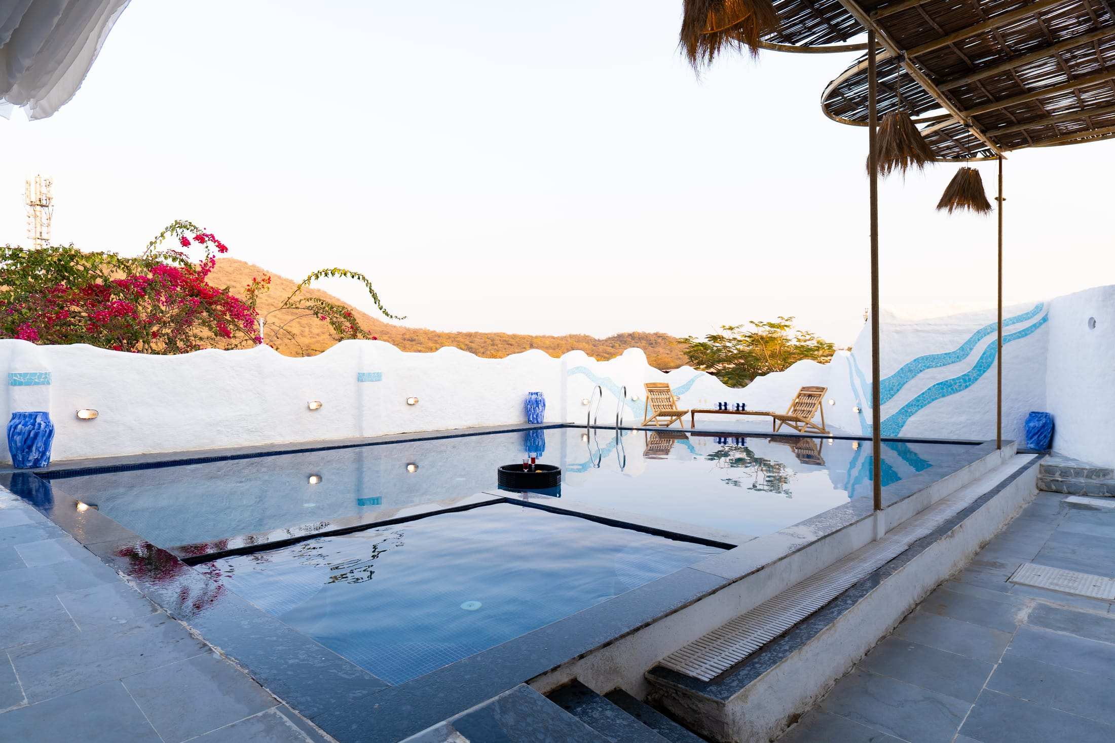 Pool edge at sunset with wavy white wall and Aravalli hills in the distance