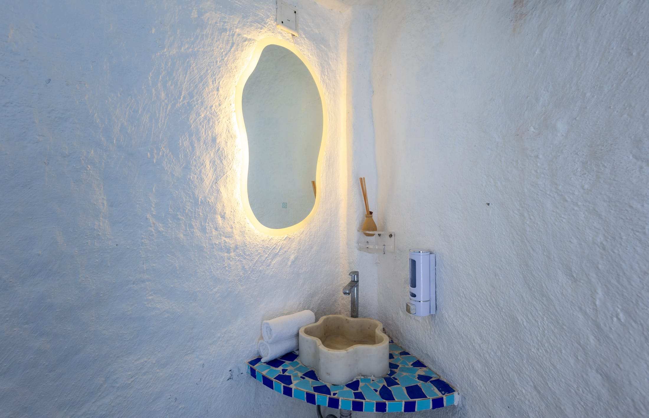 Poolside washroom with an oval backlit mirror and blue mosaic basin