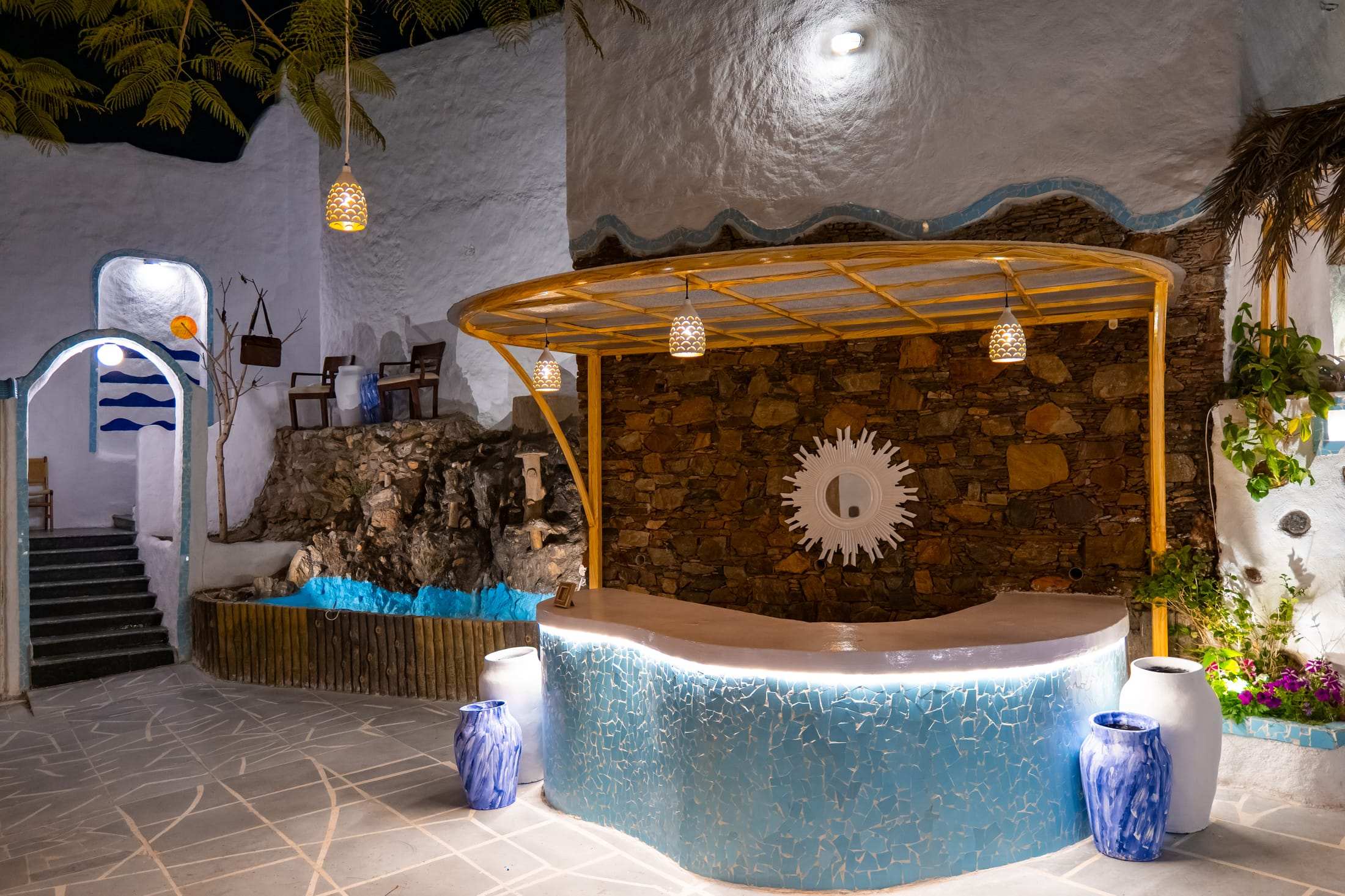 Reception desk in blue mosaic tile beneath a wooden pergola and sun motif