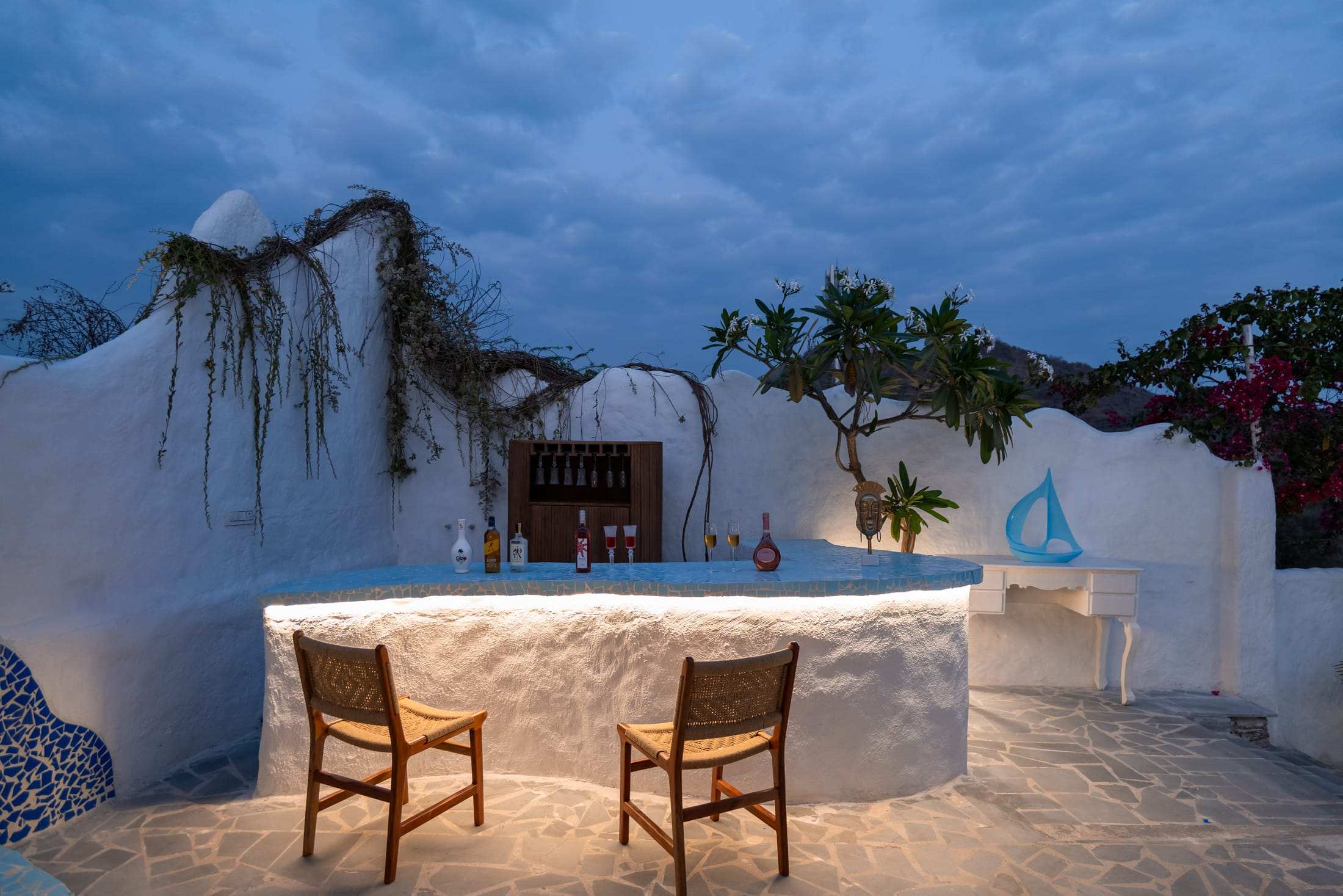 Rooftop bar counter glowing at dusk with a plumeria tree and bar stools