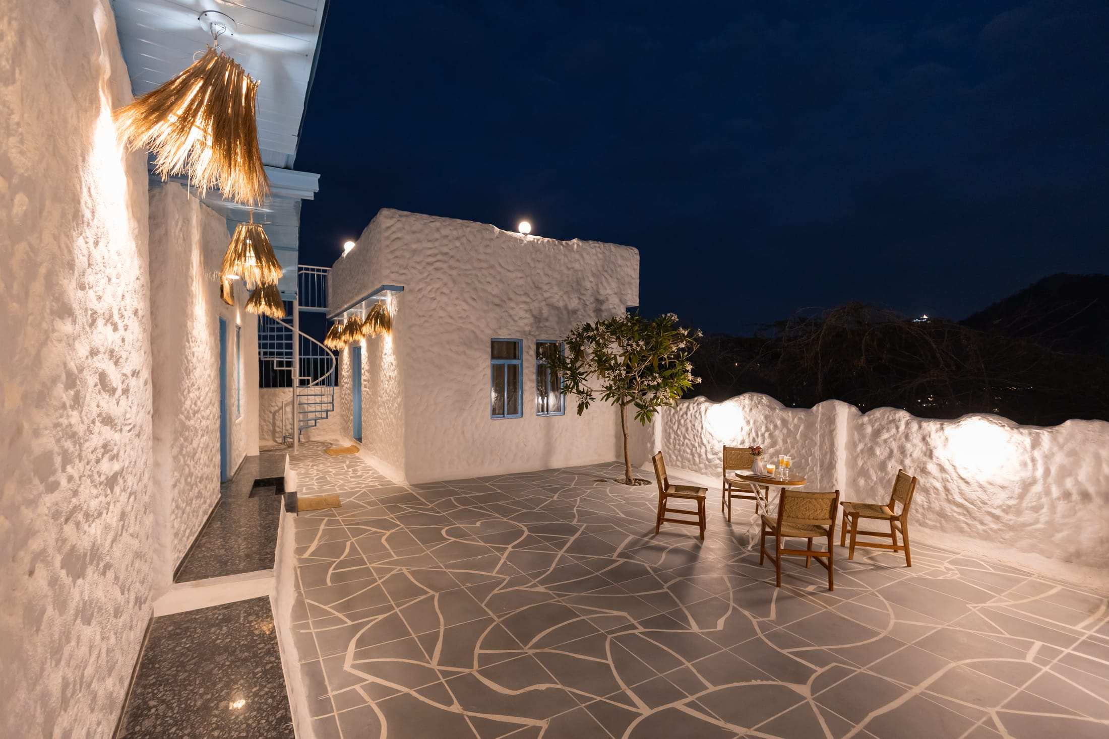 Flagstone courtyard with wooden chairs lit at night in front of the white villa