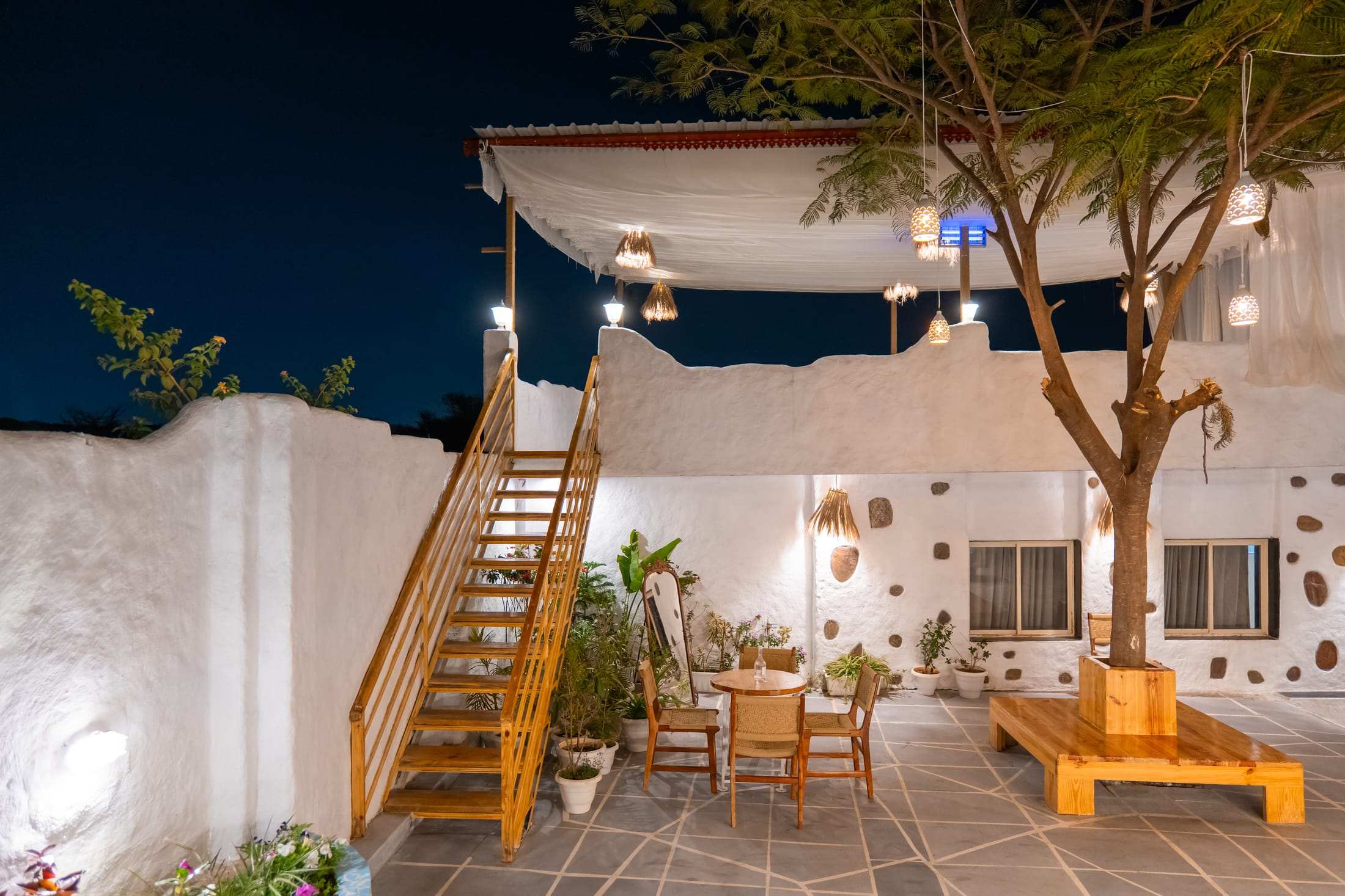 Terrace café courtyard at night with a tree, wooden staircase and lit canopy