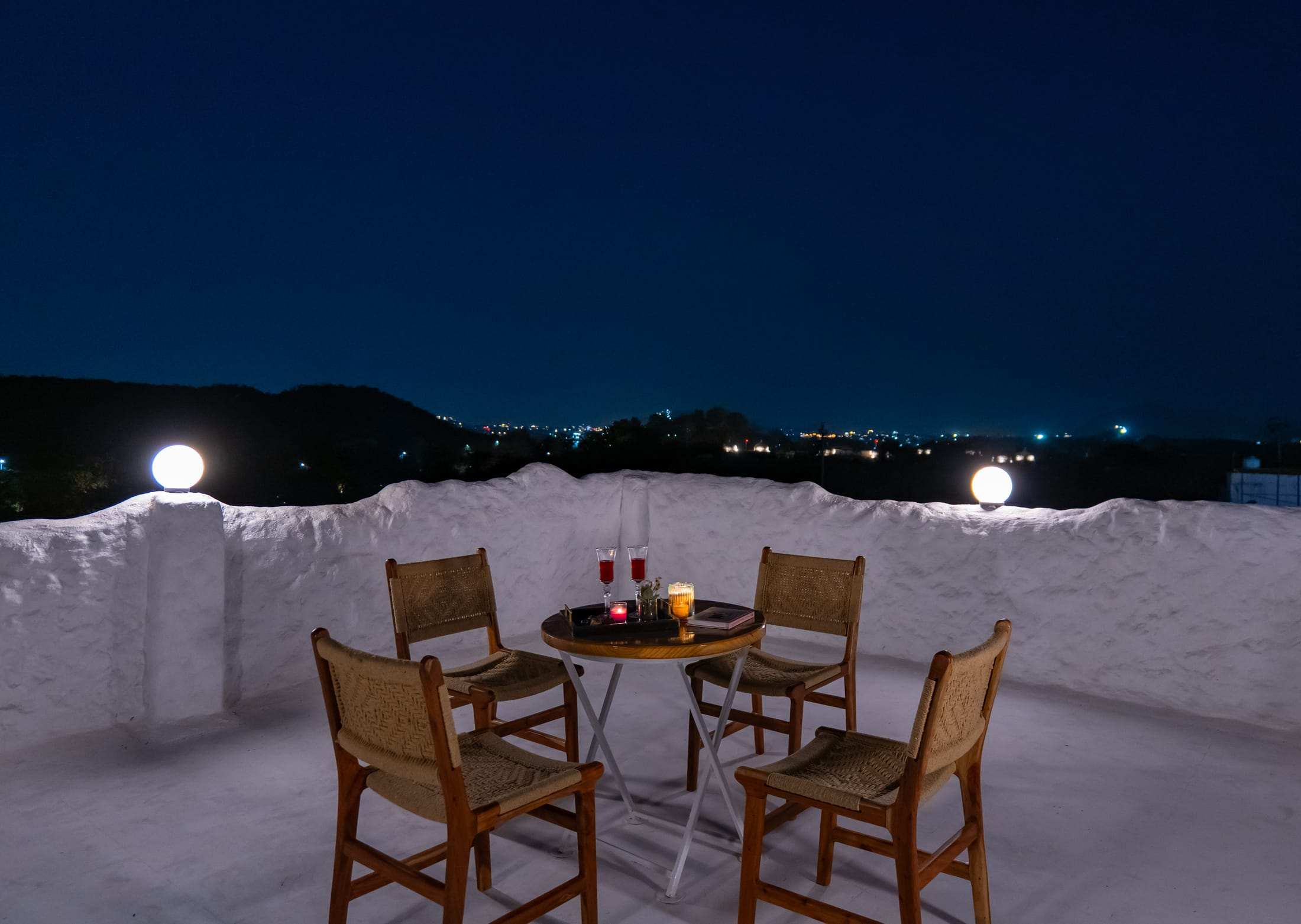 Night terrace with two chairs and distant city lights below the hills