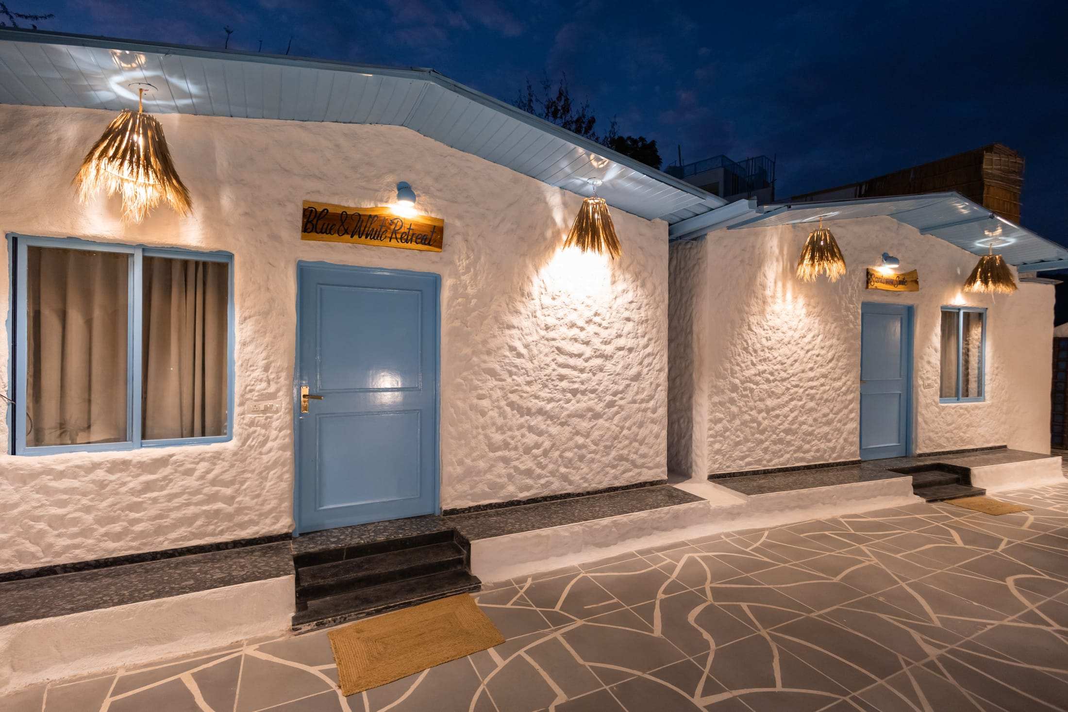 Whitewashed villa courtyard at night with warm wall lights and blue doors