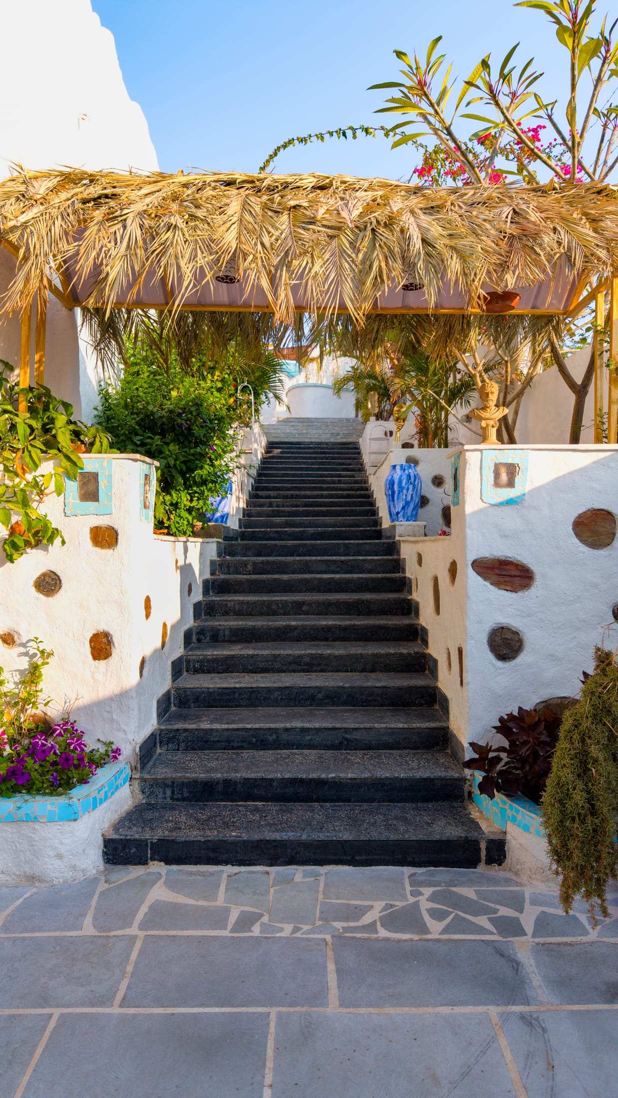 Dark stone stairway rising between whitewashed walls and flowering plants
